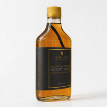 Load image into Gallery viewer, Bottle of Arbor and Field Black Label Bourbon-Infused Shagbark Hickory Syrup with black and gold foil label. A piece if bourbon-infused shagbark hickory bark can be seen inside of the bottle. The spine of the bottle reads "bottle aged with fine bourbon". Clean white background, premium look and feel.