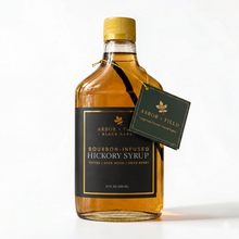 Load image into Gallery viewer, Bottle of Arbor and Field Black Label Bourbon-Infused Shagbark Hickory Syrup with black and gold foil label. A piece if bourbon-infused shagbark hickory bark can be seen inside of the bottle. A green gift tag hangs from the neck of the bottle on a gold string. Clean white background, premium look and feel.