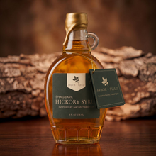 Load image into Gallery viewer, Shagbark Hickory Syrup 8 oz flask bottle with green and cream Arbor and Field Label on the front, a gold wax dipped cap and dark green gift tag hanging around the neck of the bottle from a gold string. Dark wood background, premium look and feel.
