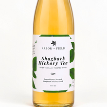 Load image into Gallery viewer, Bottle of Arbor and Field shagbark hickory tea with a green and white label. Modern clear glass wine bottle with amber colored tea inside. Clean white background, premium look and feel.
