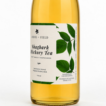 Load image into Gallery viewer, Bottle of Arbor and Field shagbark hickory tea with a green and white label. Modern clear glass wine bottle with amber colored tea inside. Clean white background, premium look and feel.
