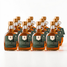 Load image into Gallery viewer, 12 bottles of Shagbark Hickory Syrup 16 oz growler bottles with green and cream Arbor and Field Label on the front, a gold wax dipped cap and dark green gift tag hanging around the neck of the bottle  from a gold string. Clean white background, premium look and feel. 
