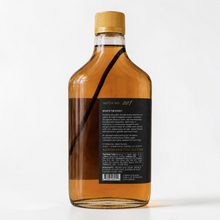 Load image into Gallery viewer, Bottle of Arbor and Field Black Label Bourbon-Infused Shagbark Hickory Syrup with black and gold foil label. A piece if bourbon-infused shagbark hickory bark can be seen inside of the bottle. The image shows the back label of the bottle with a handwritten gold batch number, pairing suggestions and a description of how the product is crafted. Clean white background, premium look and feel.
