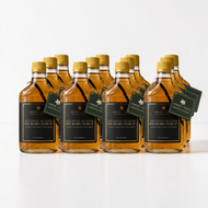 A 12 pack case of bottle of Arbor and Field Black Label Bourbon-Infused bottle aged Shagbark Hickory Syrup with black and gold foil label. A piece if bourbon-infused shagbark hickory bark can be seen inside of the bottle. A green gift tag hangs from the neck of the bottle on a gold string. Clean white background, premium look and feel.