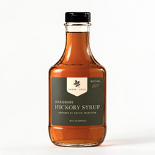 Load image into Gallery viewer, Shagbark Hickory Syrup 32 oz flask bottle with green and cream Arbor and Field Label on the front, a gold wax dipped cap and a handwritten gold batch number. Clean white background, premium look and feel. 
