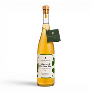 Bottle of Arbor and Field shagbark hickory tea with a wooden cork, green and white label and a green gift tag hanging from the neck by a gold string.  Modern clear glass wine bottle with amber colored tea inside. Clean white background, premium look and feel. 