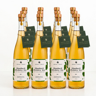 Set of 12 bottles of Arbor and Field shagbark hickory tea with wooden corks, green and white labels and a green gift tag hanging from the neck of each bottle on a gold string.  Modern clear glass wine bottles with amber colored tea inside. Clean white background, premium look and feel. 